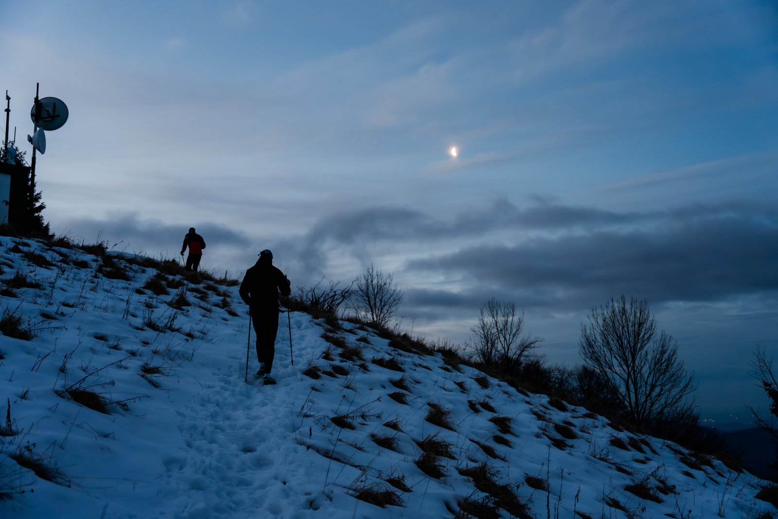 Two silhouettes hiking uphill through snow against a dramatic twilight sky, the physical metaphor for doing hard things