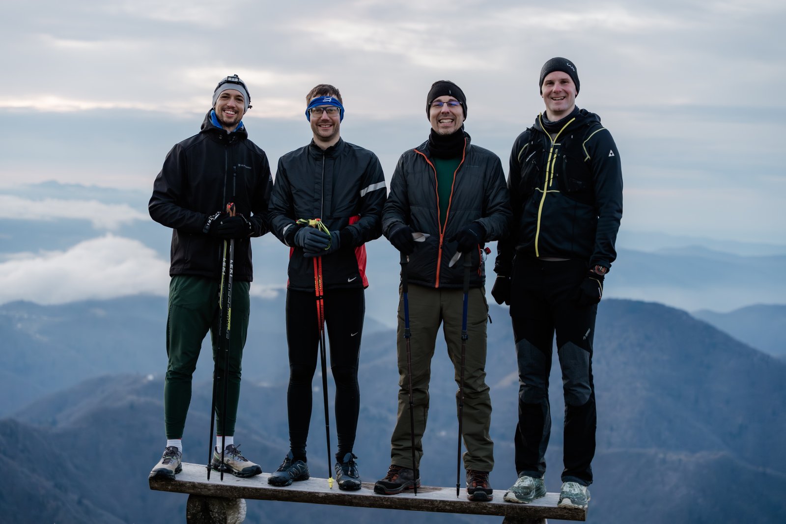 Four people standing together on a mountain summit, the shared experience of doing hard things together
