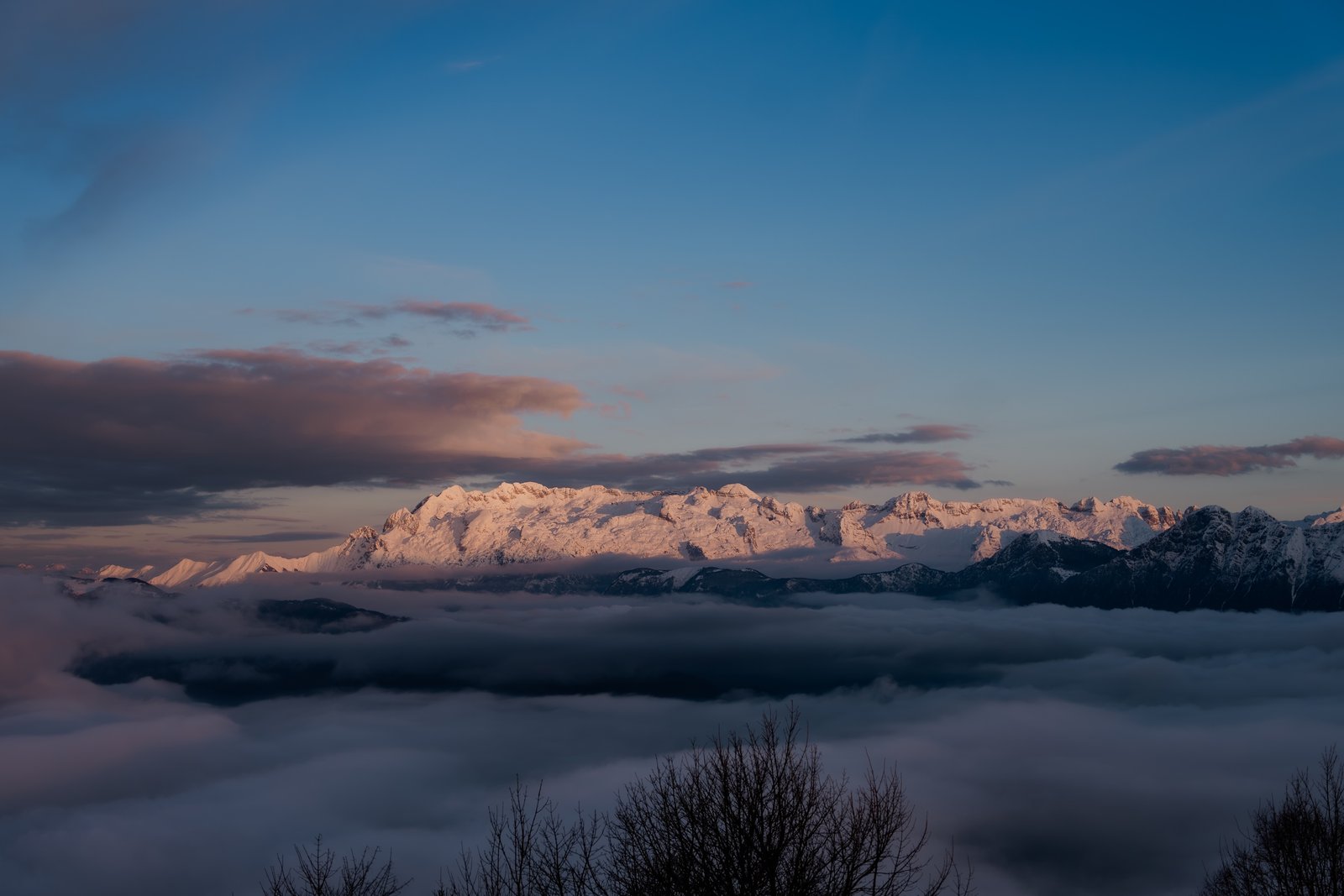 Snow-capped mountain peaks rising above a sea of clouds at sunset, pure nature without distraction